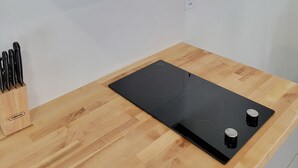 Une cuisine équipée d’un four à micro-ondes encastré, d’une plaque de cuisson à induction noire et d’un bloc à couteaux posé sur un plan de travail en bois.