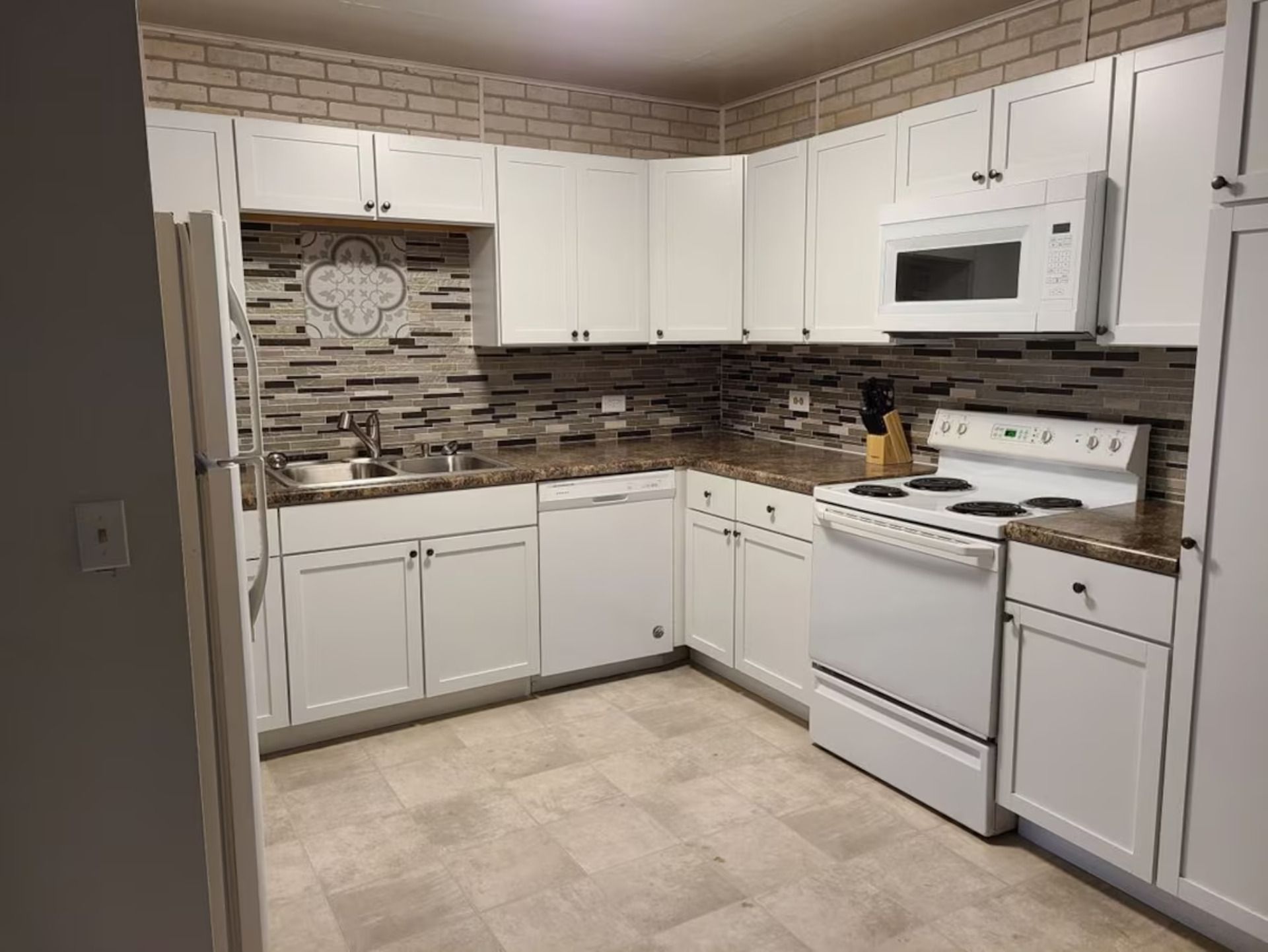A kitchen with white cabinets, a microwave, a stove, and a tiled backsplash.
