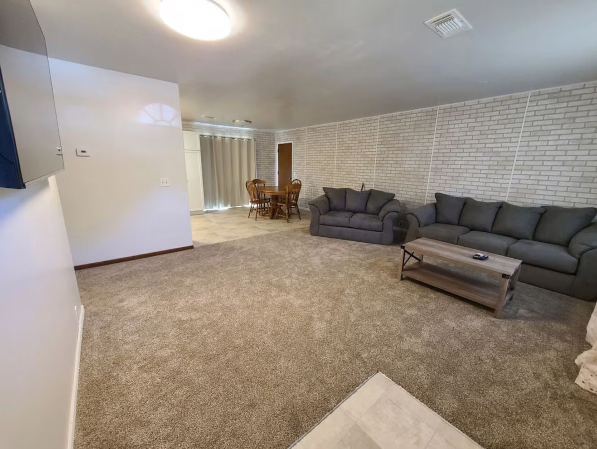 A living room with a carpeted floor, a sofa, a coffee table, and a dining area with chairs and a table.