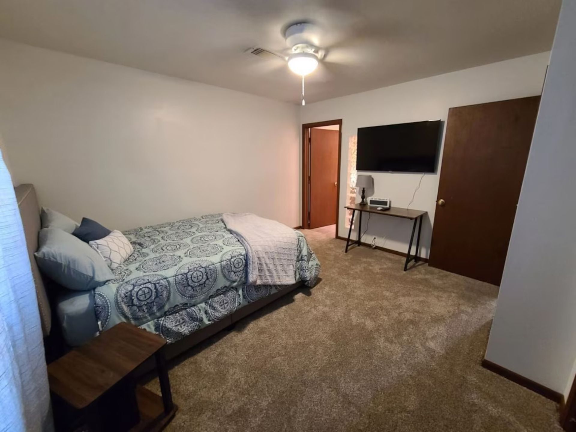 A bedroom with a bed, a desk, a television, and a ceiling fan.