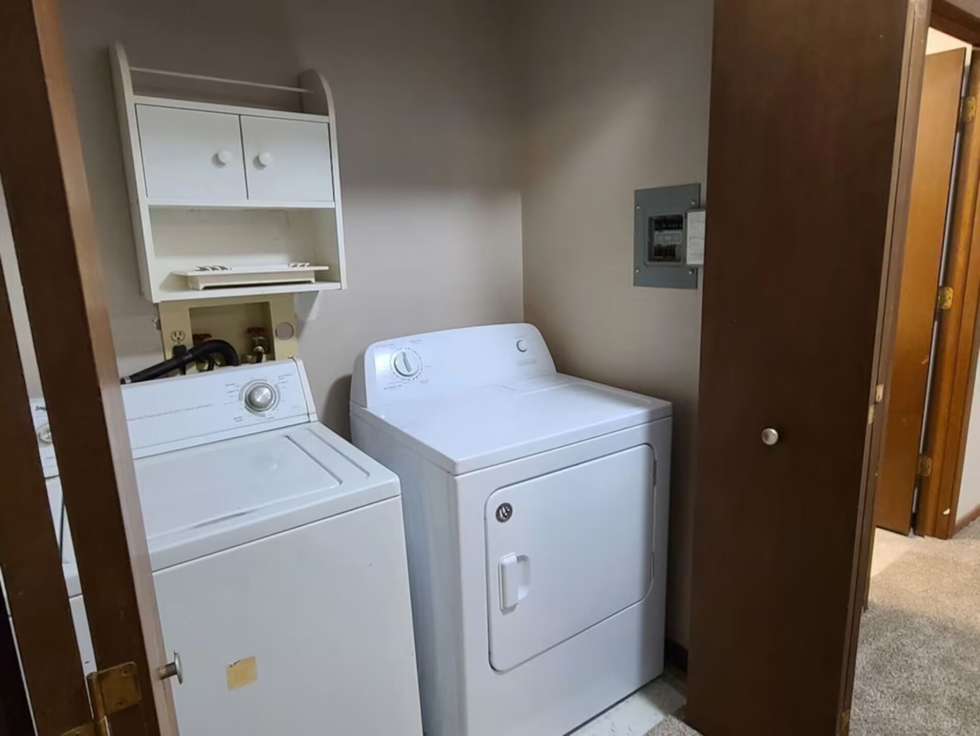 A laundry room with a washer and dryer, a shelf above the washer, and a door leading to another room.