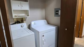 A laundry room with a washer and dryer, a shelf above the washer, and a door leading to another room.