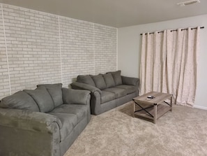 A living room with a sectional sofa, a coffee table, and a brick-patterned wall.