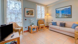 A living room with a television, wicker chairs, a sofa, a small table with a plant, and a painting on the wall. - Porto Letizia Orchidea 3, Porlezza, Italy (Porlezza)