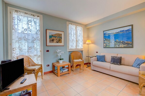 A living room with a television, wicker chairs, a sofa, a small table with a plant, and a painting on the wall. - Porto Letizia Orchidea 3, Porlezza, Italy (Porlezza)