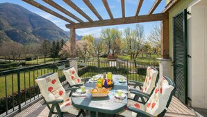 A covered outdoor dining area with a table set for four, surrounded by chairs with heart-patterned cushions. - Porto Letizia Orchidea 3, Porlezza, Italy (Porlezza)