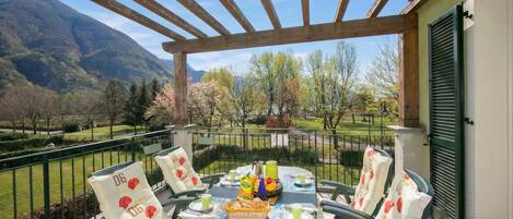 A covered outdoor dining area with a table set for four, surrounded by chairs with heart-patterned cushions.