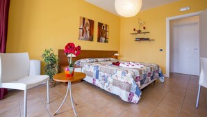 Een slaapkamer met twee bedden, een zithoek met een stoel en een tafel, een kamerplant en kunst aan de muur.