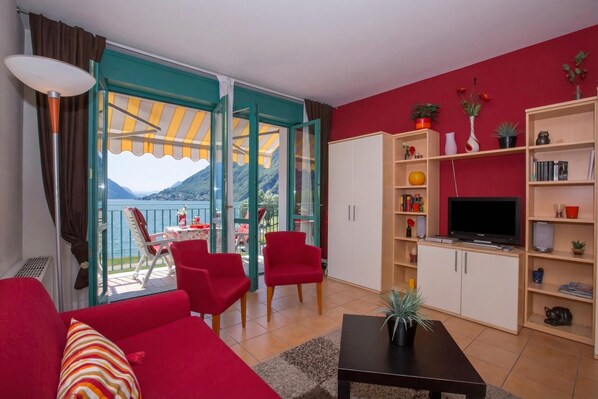 A living room with a red sofa, a TV, and a bookshelf. - Porto Letizia S12, Porlezza, Italy (Porlezza)