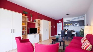 Een moderne woonkamer met rode banken, een televisie en een keuken op de achtergrond.