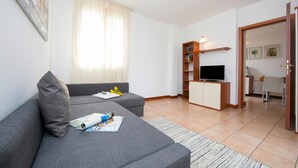 A modern living room with a grey sofa, a flat-screen TV, a bookshelf, and a dining area with a table and chairs. - Porto Letizia Begonia 6, Porlezza, Italy (Porlezza)