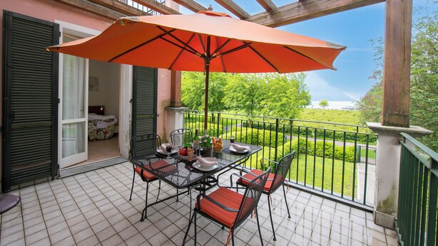 A balcony with a table, chairs, and an umbrella. - Porto Letizia Begonia 6, Porlezza, Italy (Porlezza)