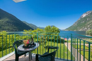 A balcony with a table and chairs overlooking a lake and mountains. - Porto Letizia S14, Porlezza, Italy (Porlezza)