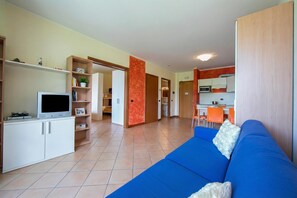 Un soggiorno moderno con un divano blu, una TV a schermo piatto e un angolo cucina sullo sfondo.
