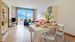 A modern living room with a dining area, a bookshelf, a TV, and a view of the sea. - Porto Letizia P14, Porlezza, Italy (Porlezza)