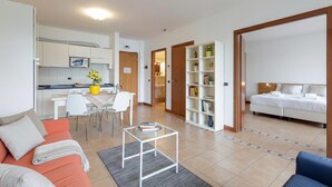 A modern apartment with a living room, kitchen, and bedroom. It includes a sofa, a coffee table, a dining area, and a bookshelf. - Porto Letizia P14, Porlezza, Italy (Porlezza)