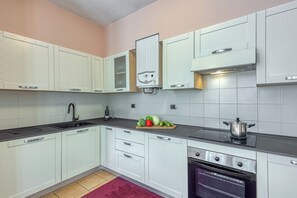 Una cucina moderna con mobili bianchi, un piano di lavoro nero, un forno integrato e uno scaldabagno a vista.