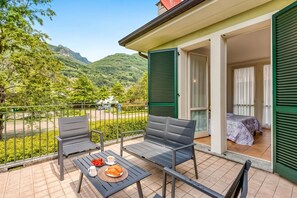 A balcony with two chairs and a table, a bed with a view, and a mountain backdrop. - Porto Letizia Rosa 2, Porlezza, Italy (Porlezza)