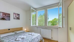 A bedroom with a bed, two wall-mounted pictures, a window with a view of trees, and a radiator. - Porto Letizia Rosa 2, Porlezza, Italy (Porlezza)