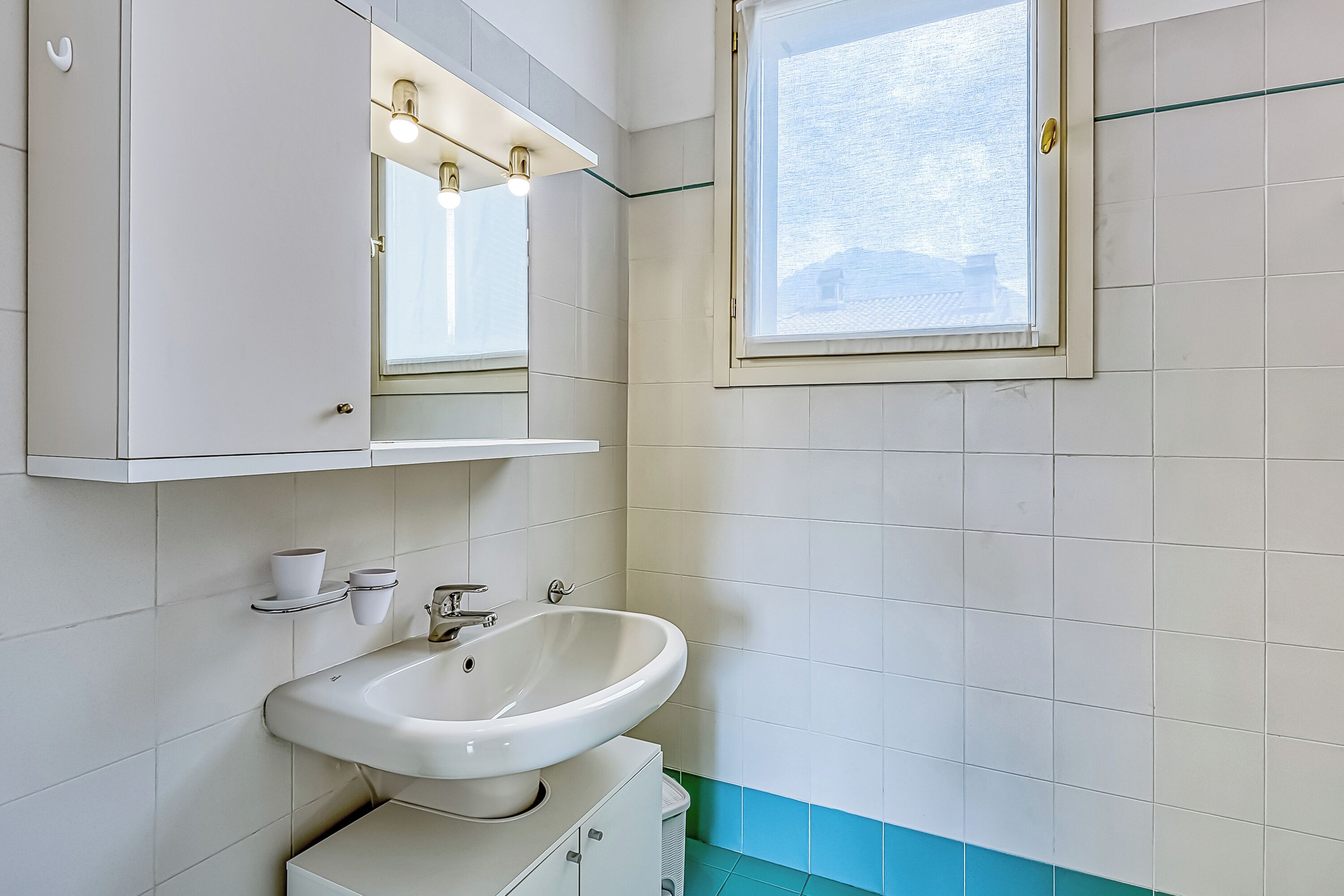 Une salle de bain avec un lavabo blanc, un miroir au-dessus et une fenêtre.
