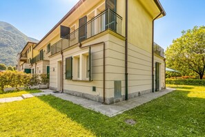 Un edificio residenziale a due piani con un balcone, un giardino e una montagna sullo sfondo.
