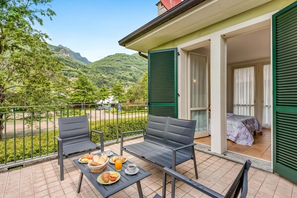 A balcony with a table set for breakfast, chairs, and a view of a mountainous landscape.
