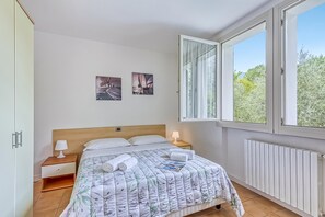 Ein Schlafzimmer mit einem Bett, zwei Nachttischlampen, einem Fenster mit Vorhängen und zwei Wandbildern.