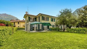 A two-story house with a balcony, a patio with a table and chairs, and a green umbrella. - Porto Letizia Rosa 2, Porlezza, Italy (Porlezza)