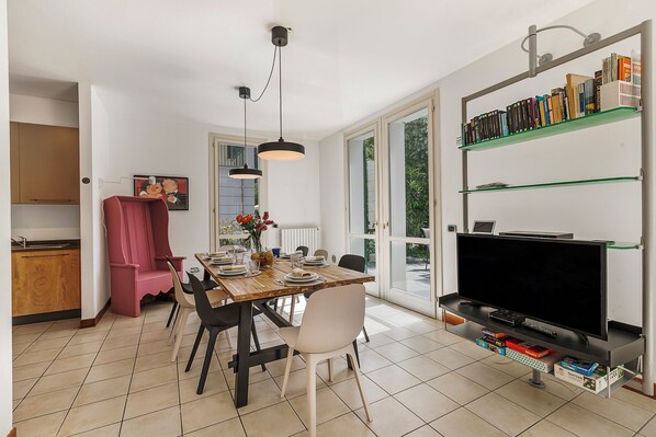 Un salon moderne comprenant un coin repas, un téléviseur posé sur un meuble et une bibliothèque.