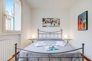 A neatly made bed with a quilted bedspread, two bedside lamps, and a painting above it.