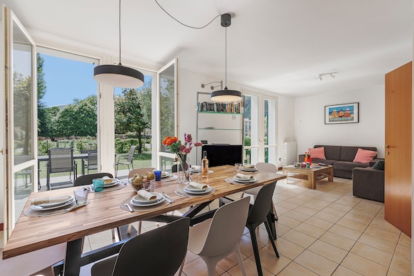Un coin repas avec une table en bois dressée pour quatre personnes, entourée de chaises, et une bibliothèque en arrière-plan.