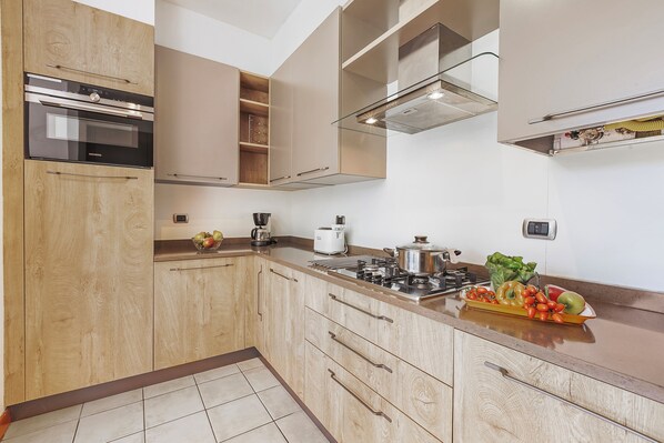 A modern kitchen with wooden cabinets, stainless steel appliances, and a countertop with fruits and vegetables. - Porto Letizia Rosa 1, Porlezza, Italy (Porlezza)