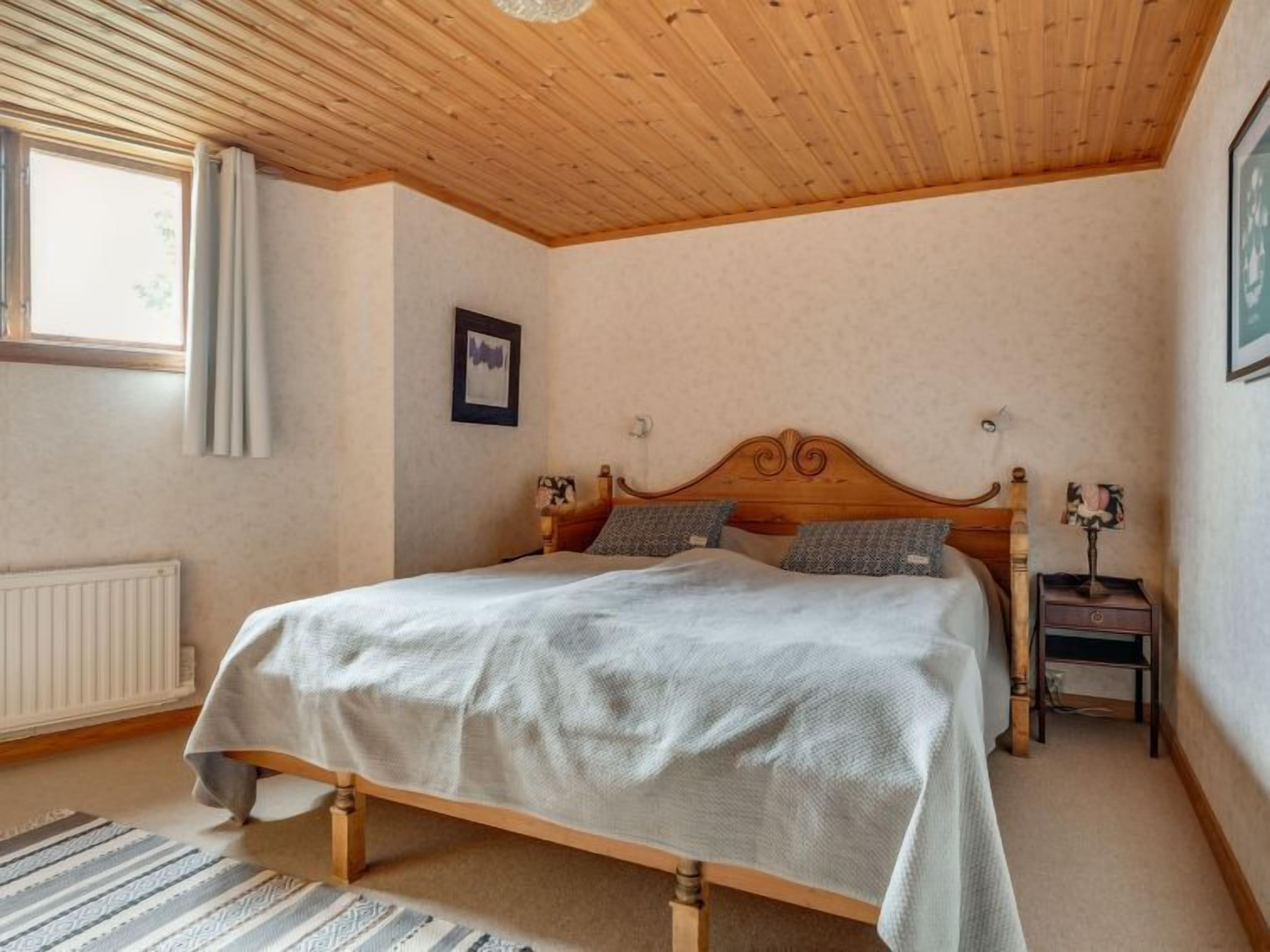 Une chambre à coucher avec un lit en bois, un radiateur, une fenêtre avec des rideaux et une table de chevet avec une lampe.