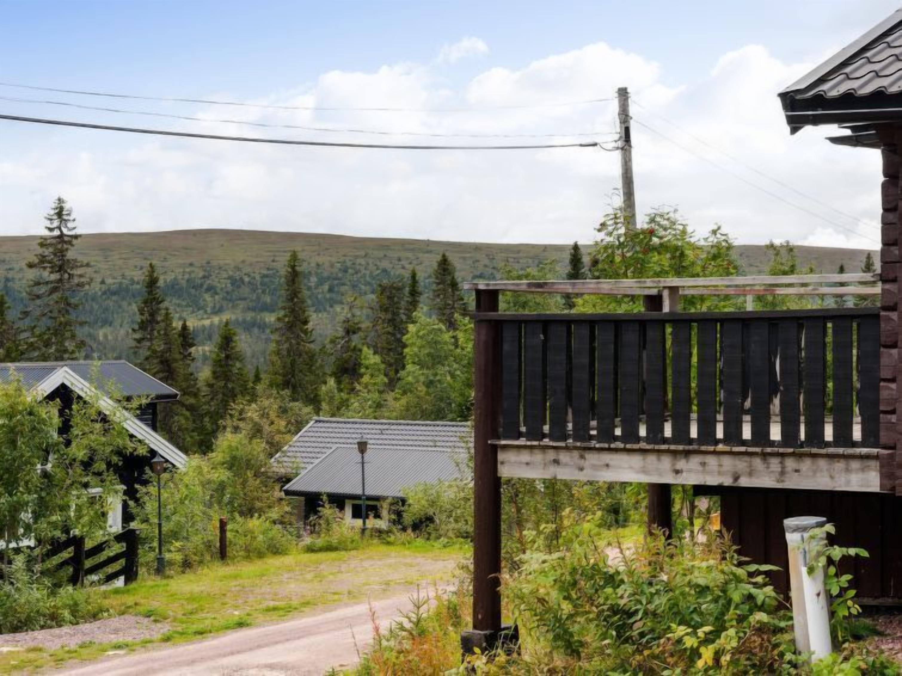 En rustik stuga med en träveranda, omgiven av tät skog och kullar.
