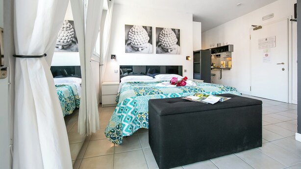 Ein modernes Schlafzimmer mit zwei Betten, einem schwarzen Pouf und einem großen Fenster mit Vorhängen.