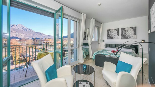 A modern hotel room with a balcony, a bed with a floral bedspread, and a view of mountains. - Porto Letizia T1, Porlezza, Italy (Porlezza)