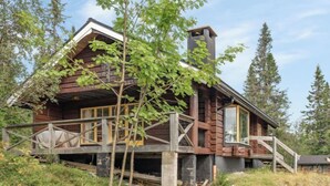 Eine Holzhütte mit Balkon, umgeben von Bäumen und einer Rasenfläche.