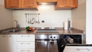 Cuina amb armaris de fusta, un rentatalls d'acer inoxidable, forn encastrat i màquina d'esbandir plats.