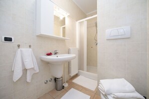 A bathroom with a sink, mirror, shower, and towel rack.
