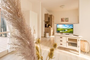 A modern living room with a flat-screen TV, a white entertainment unit, and a view of a green landscape through the window. - Porto Letizia Mimosa 3, Porlezza, Italy (Porlezza)