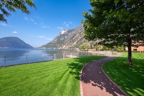 A park with a paved path, a lake, and mountains in the background.