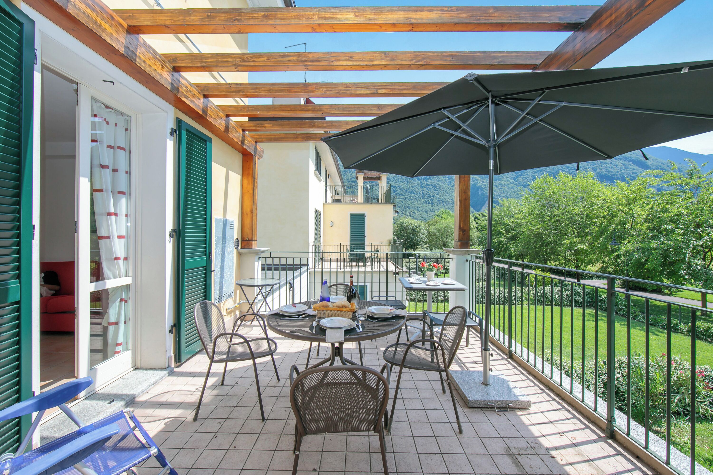 A covered patio with a table and chairs, a large umbrella, and a view of a mountain.