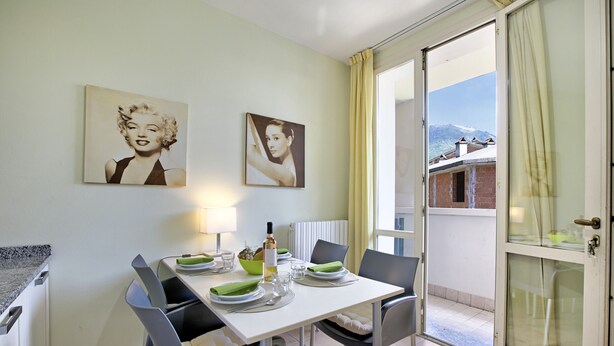 A dining area with a white table set for two, two framed pictures on the wall, and a view of a mountain through an open door. - Porto Letizia Begonia 5, Porlezza, Italy (Porlezza)