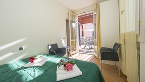 A hotel room with a green bedspread, a small table with a chair, and a balcony with a table and chairs. - Porto Letizia Begonia 5, Porlezza, Italy (Porlezza)