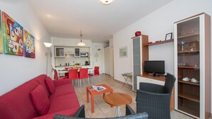 A modern living room with a red sofa, a dining area with red chairs, a kitchen with white cabinets, and a television on a wooden cabinet. - Porto Letizia T13, Porlezza, Italy (Porlezza)