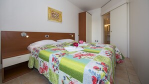 A bedroom with a wooden headboard, a floral bedspread, a bedside table with a lamp, and a door leading to another room. - Porto Letizia T13, Porlezza, Italy (Porlezza)