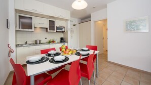 A modern kitchen with white cabinets, a microwave, and a dining area with red chairs and a white table set for two. - Porto Letizia T13, Porlezza, Italy (Porlezza)