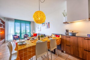 A dining area with a table set for four, a kitchen with wooden cabinets, and a large window with curtains.