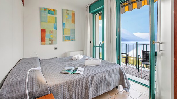 Une chambre d’hôtel avec un lit, un coin lecture, un balcon donnant sur la mer et un tableau au mur.