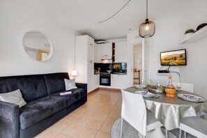 A modern living room with a black sofa, a dining table set for two, and a kitchen in the background. - Porto Letizia P9, Porlezza, Italy (Porlezza)